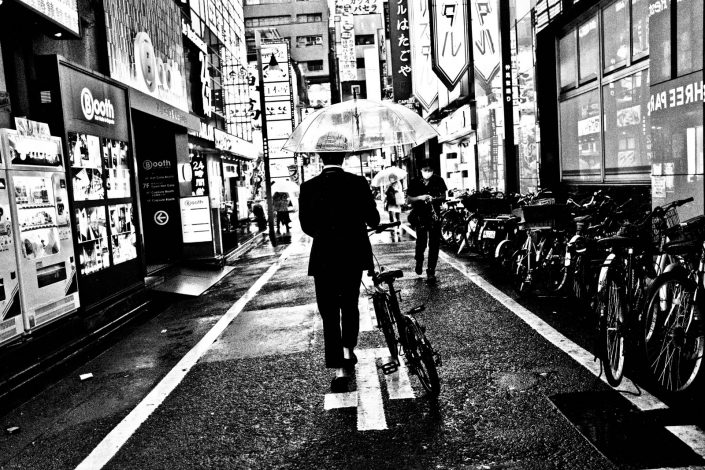 Shinjuku in the rain, Japanese man with bike and umbrella. Street Photography by Victor Borst