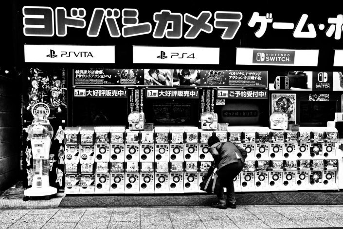 A Japanese man trying to get a toy out of a Gashapon machine. Street photography by Victor Borst