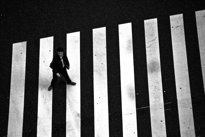 Japanese man crossing a crossover totally in monochrome. Street photography by Victor Borst