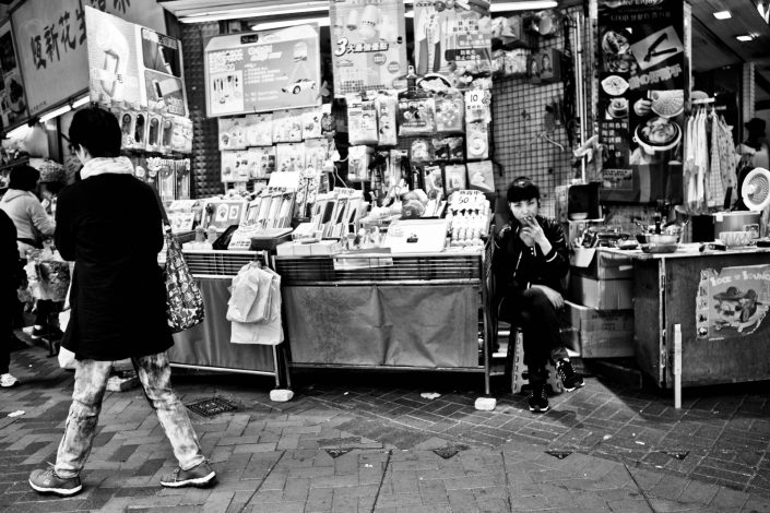 Smoking girl at a shop in Hong Kong. She looks a bit mean. Street Photography by Victor Borst