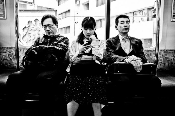 In the metro of tokyo. A girl is playing with her smartphone, one guy is sleeping and one notice me. Street photography by Victor Borst