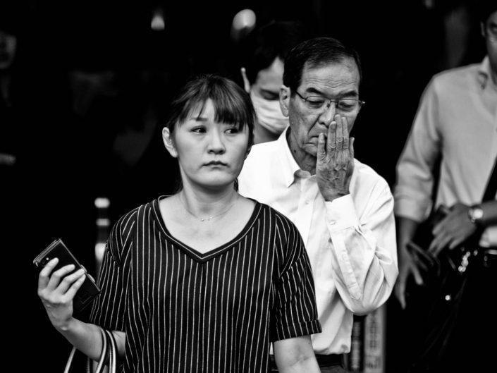 Salaryman and woman portrait. Woman with smartphone, man with hand in front of his mouth. Street Photography by Victor Borst