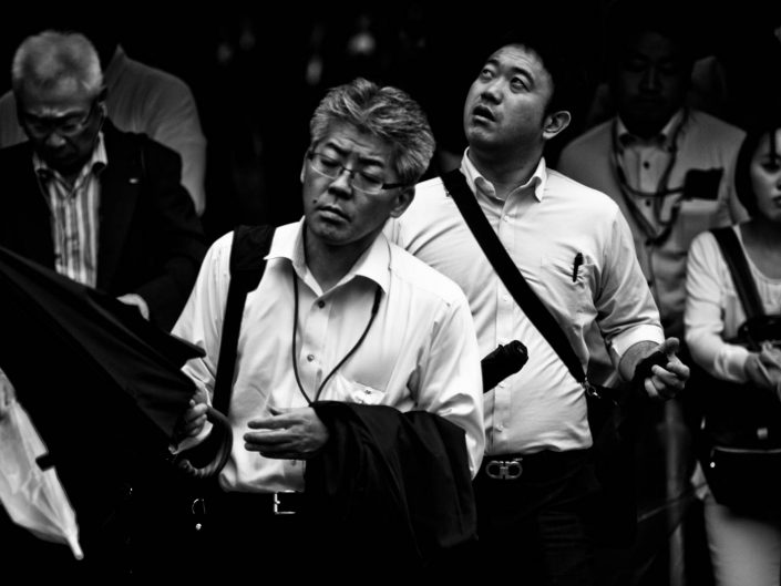 Salarymen exiting Shimbashi station watching for the rain with umbrella. Street Photography by Victor Borst