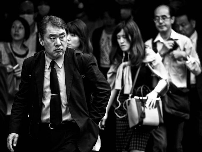 Japanese man looking to his right in a crowd at Shimbashi Station. Street Photography by Victor Borst