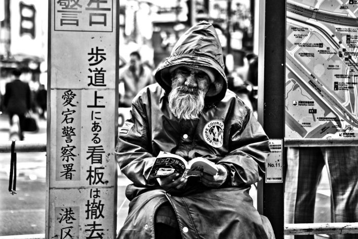Japanese Homeless at Shimbashi Station, Tokyo. He is reading a manga. Street Photography by Victor Borst